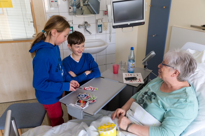 Zwei Kinder bei einer Frau am Krankenbett