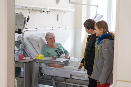 Frau im Krankenhaus wird von 2 Kindern besucht