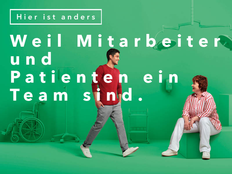 Bild mit der Aufschrift „Weil Mitarbeiter und Patienten ein Team sind.“. Ein junger Mann geht lächelnd auf eine lächelnde sitzende Frau zu. Der Hintergrund ist grün. 